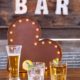 Beer Pilsner & Carat Rocks Glasses On Whiskey Barrel Bar With Barnwood Decor Wall & Bar Sign